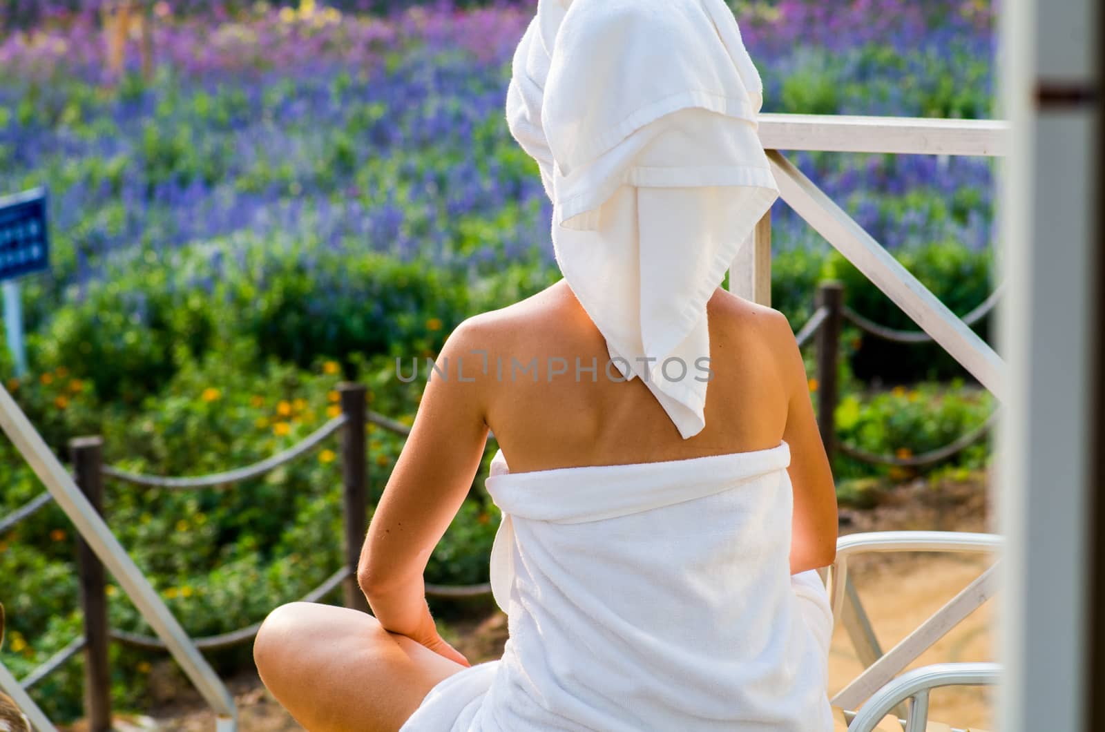 a woman in a bath towel is sitting on a lounge on a terrace looking ot the flowers