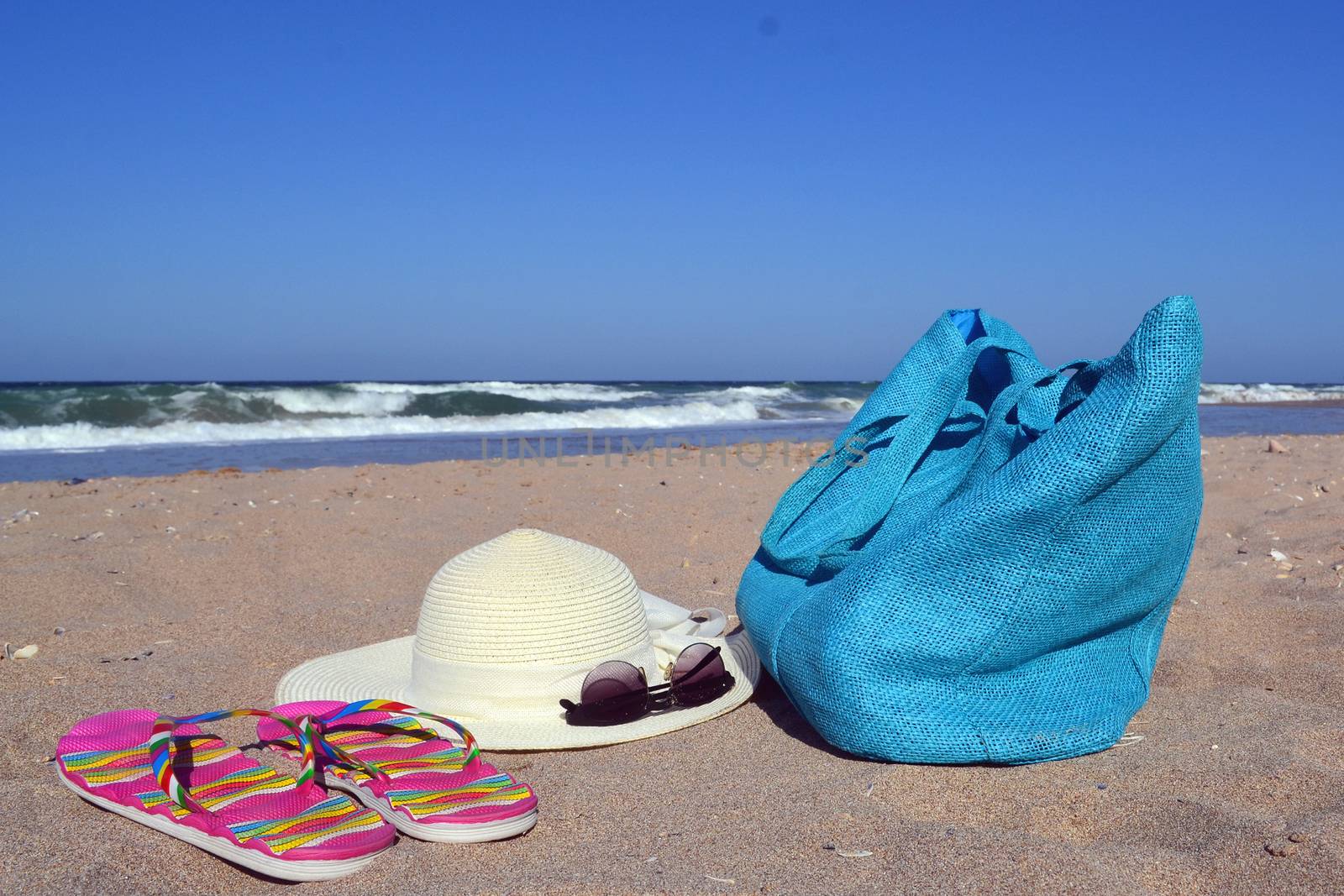 Summer concept with bag, hat, glasses and flip flops on beach by hibrida13