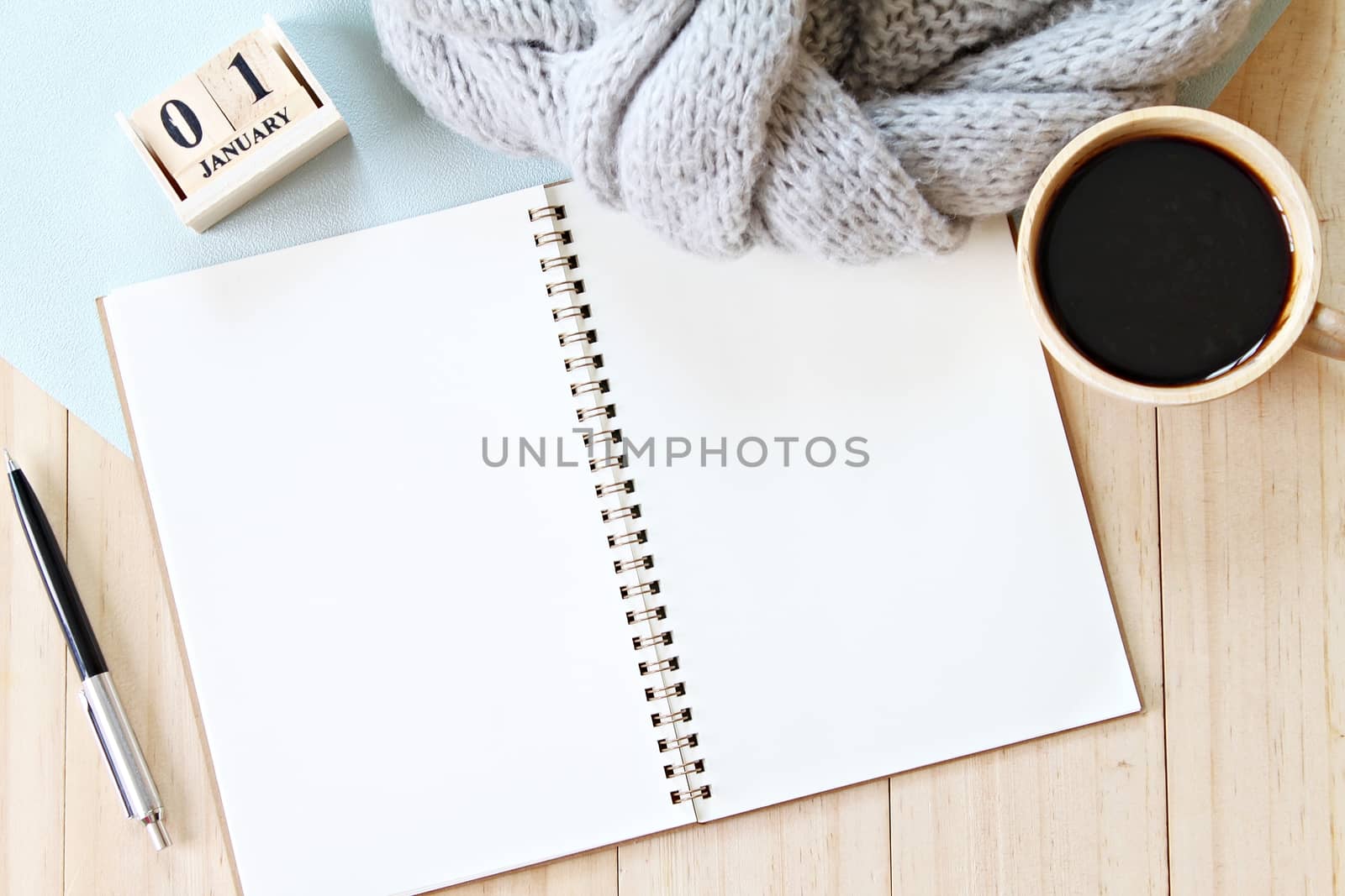 Business, weekend, holiday or new year planning concept : Flat lay or top view of gray knitted scarf, open blank notebook paper, coffee cup and new year cube calendar on wooden background