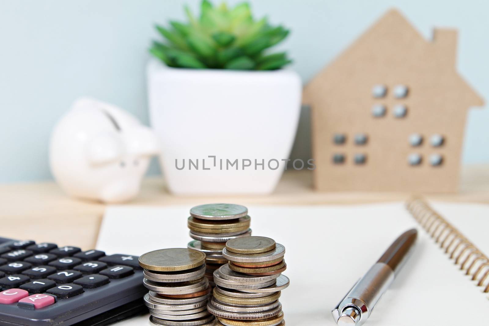 Business, finance, savings, property ladder or mortgage concept : Coins stack and calculator in front of wood house model and piggy bank