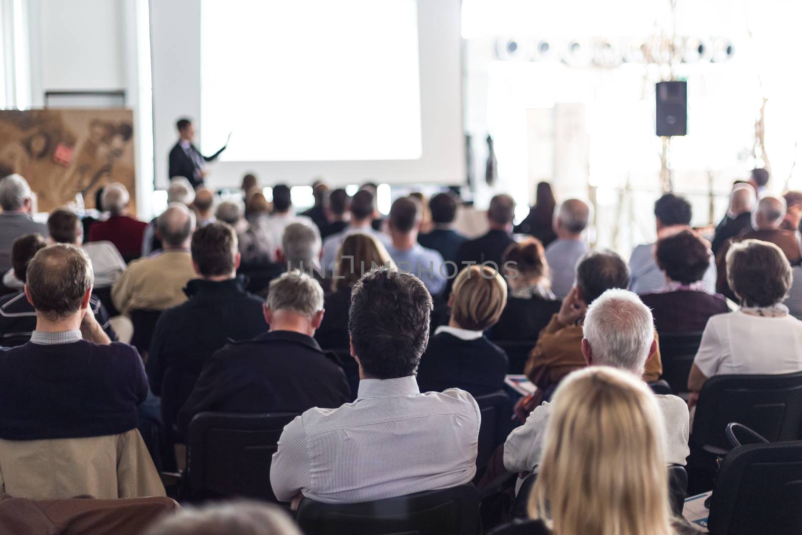 Speaker giving a talk in conference hall at business event. Audience at the conference hall. Business and Entrepreneurship concept. Focus on unrecognizable man in the audience.