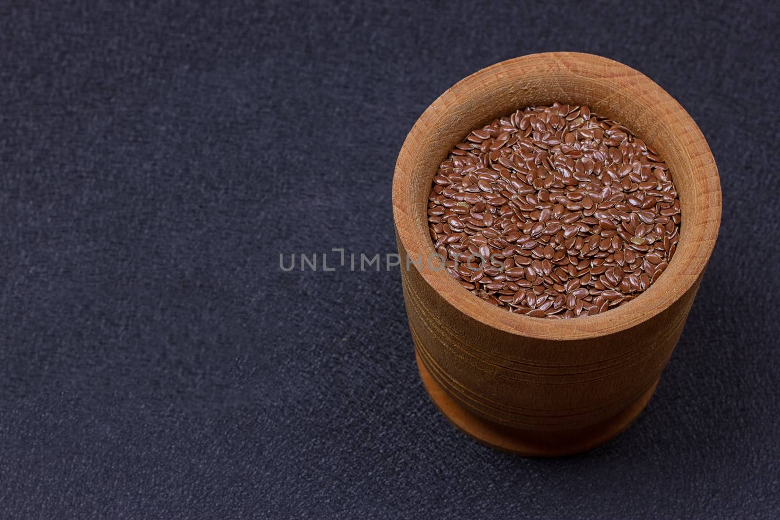 Flax seed in a wooden bowl on a black background