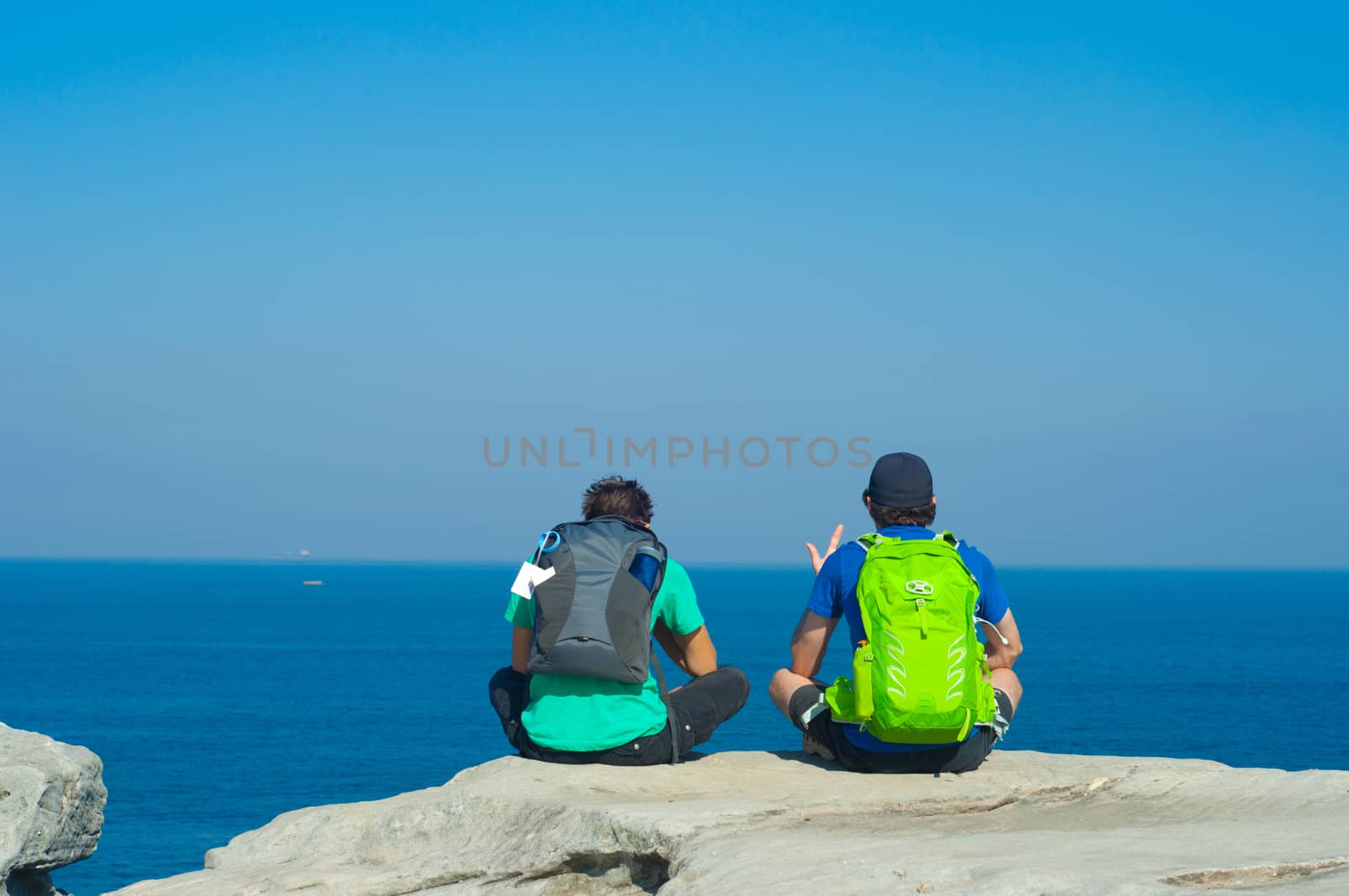 Portrait from behind of young men sitting and looking on Sea with backpack. Concept for travel or freedom.