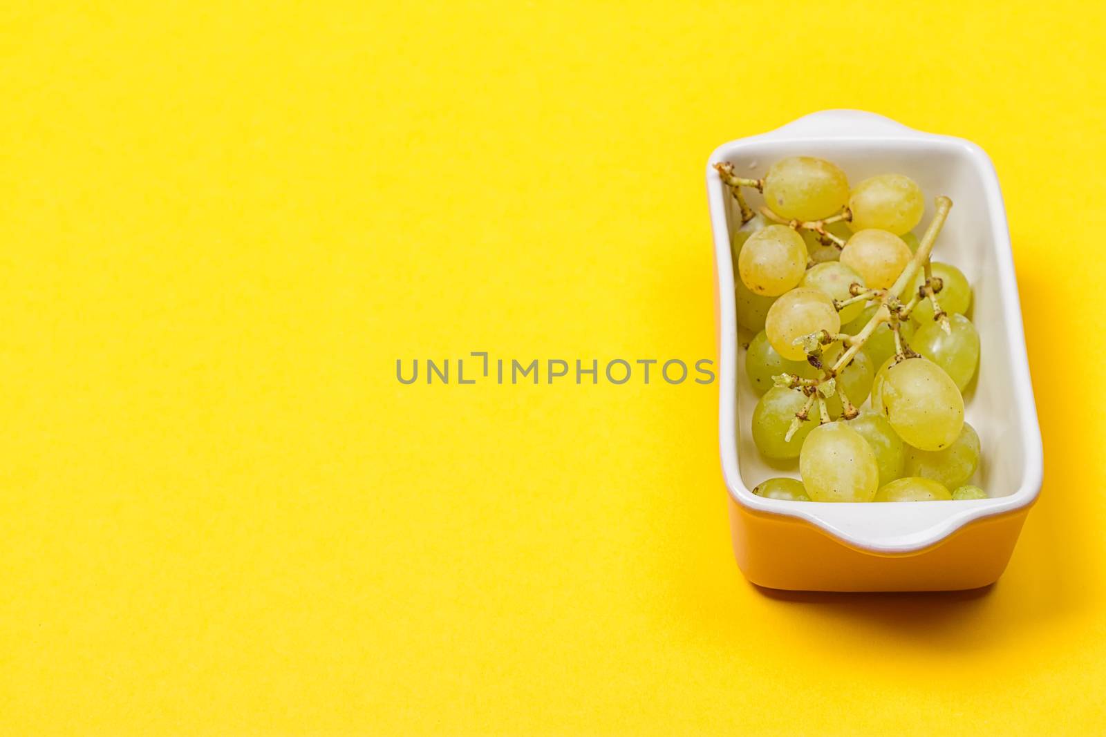 Grapes in a ceramic bowl on yellow background. Green grapes Kish Mish. Top view. copy-space