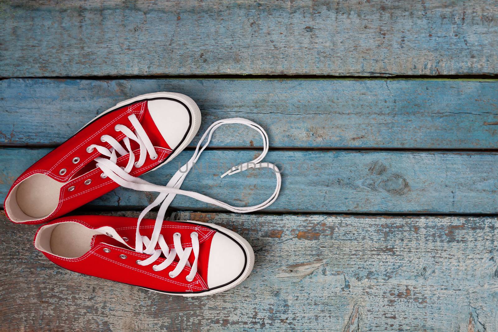 A pair of red retro sneakers on a blue wooden background, laces lined in a heart shape. Concept of young hipster love.