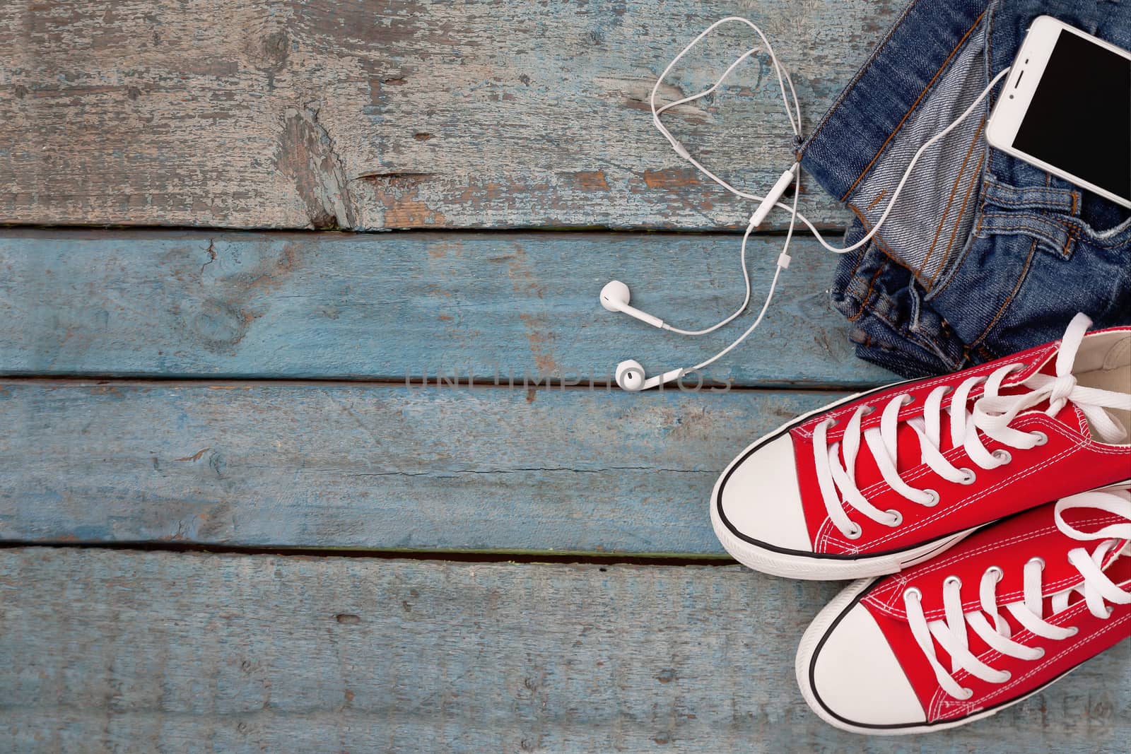 Red retro sneakers and smartphone with headset-earphones in a pocket djintsi on a blue wooden background.