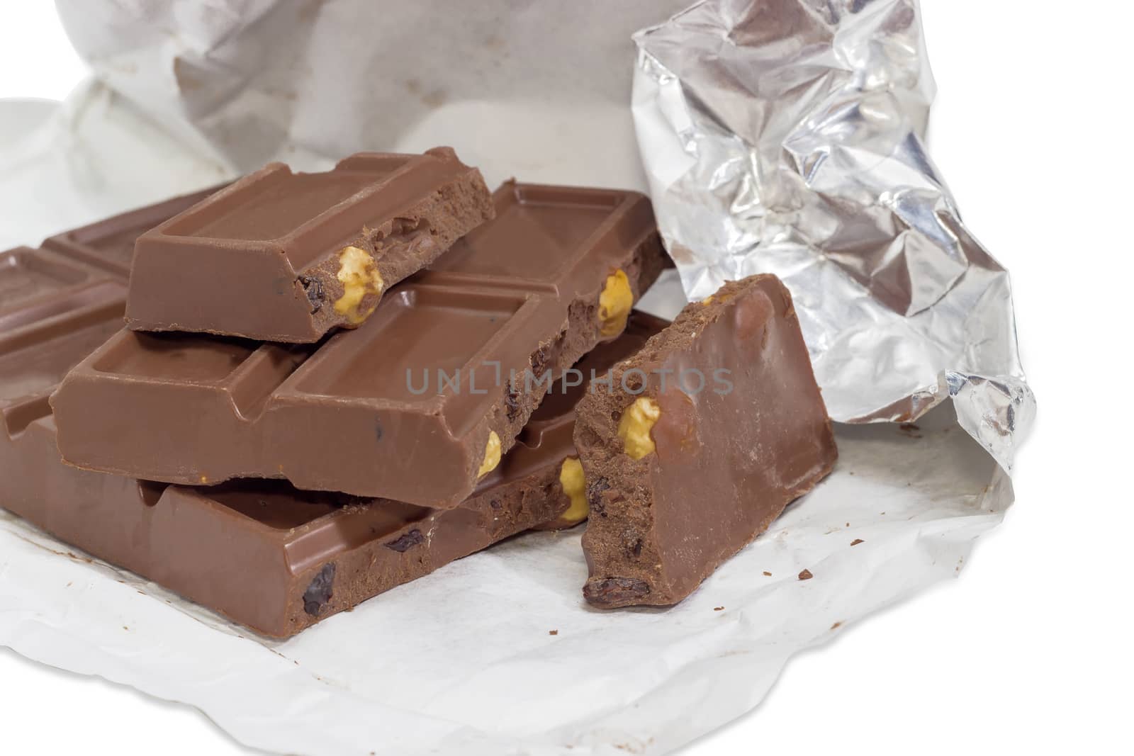 Several pieces of the milk chocolate bar with nuts and raisins in open foil wrapper closeup on a white background
