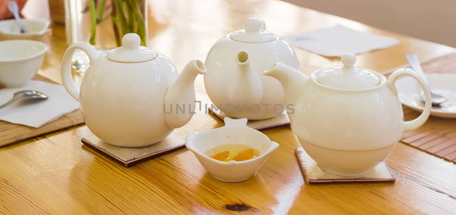 Panorama of the three white teapot on a ceramic trivets on a wooden table on a background of a tea appliances
