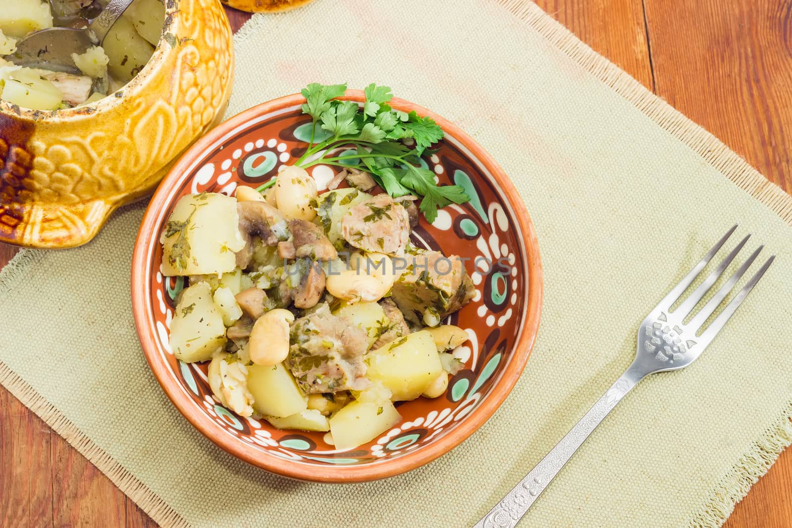 Top view of the Ukrainian version of the dish Chanakhi in a clay bowl on a napkin - potatoes with meat, mushrooms and haricot beans baked in a clay pot 
