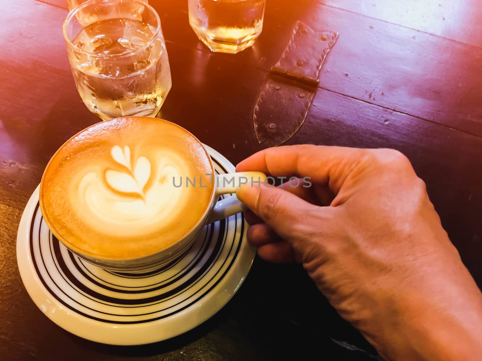 Cappuccino and water on the table with glass of water and hand