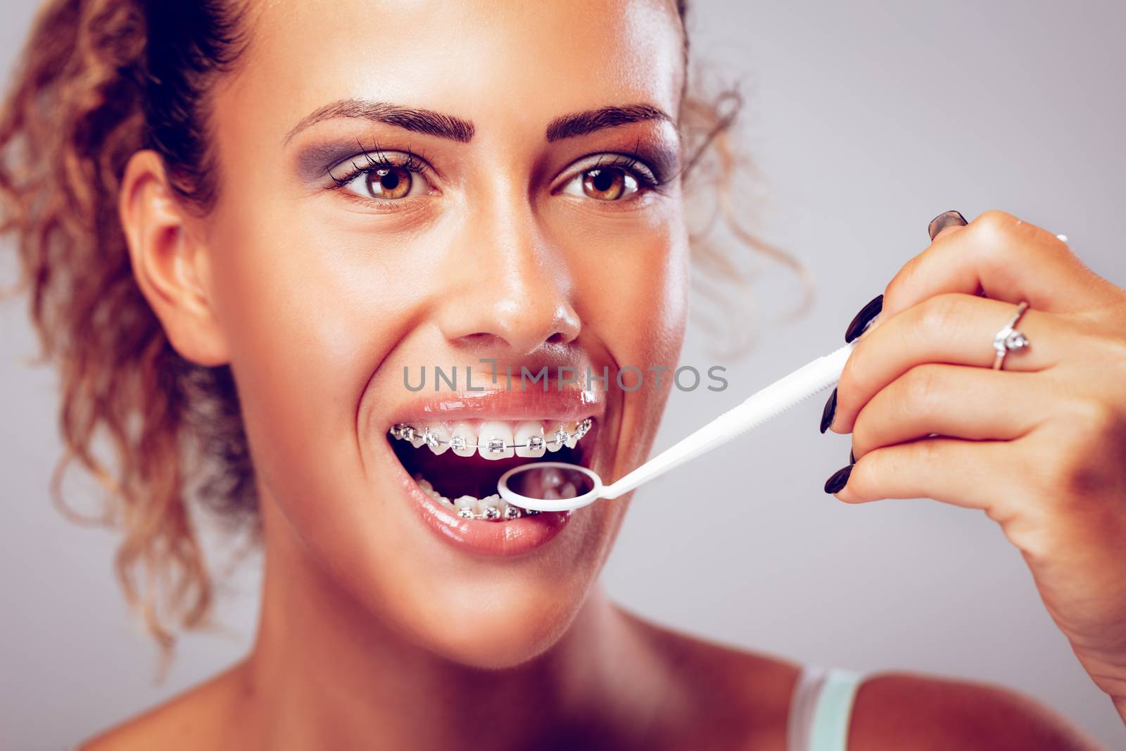 Smiling young woman checking braces with a dental mirror. 