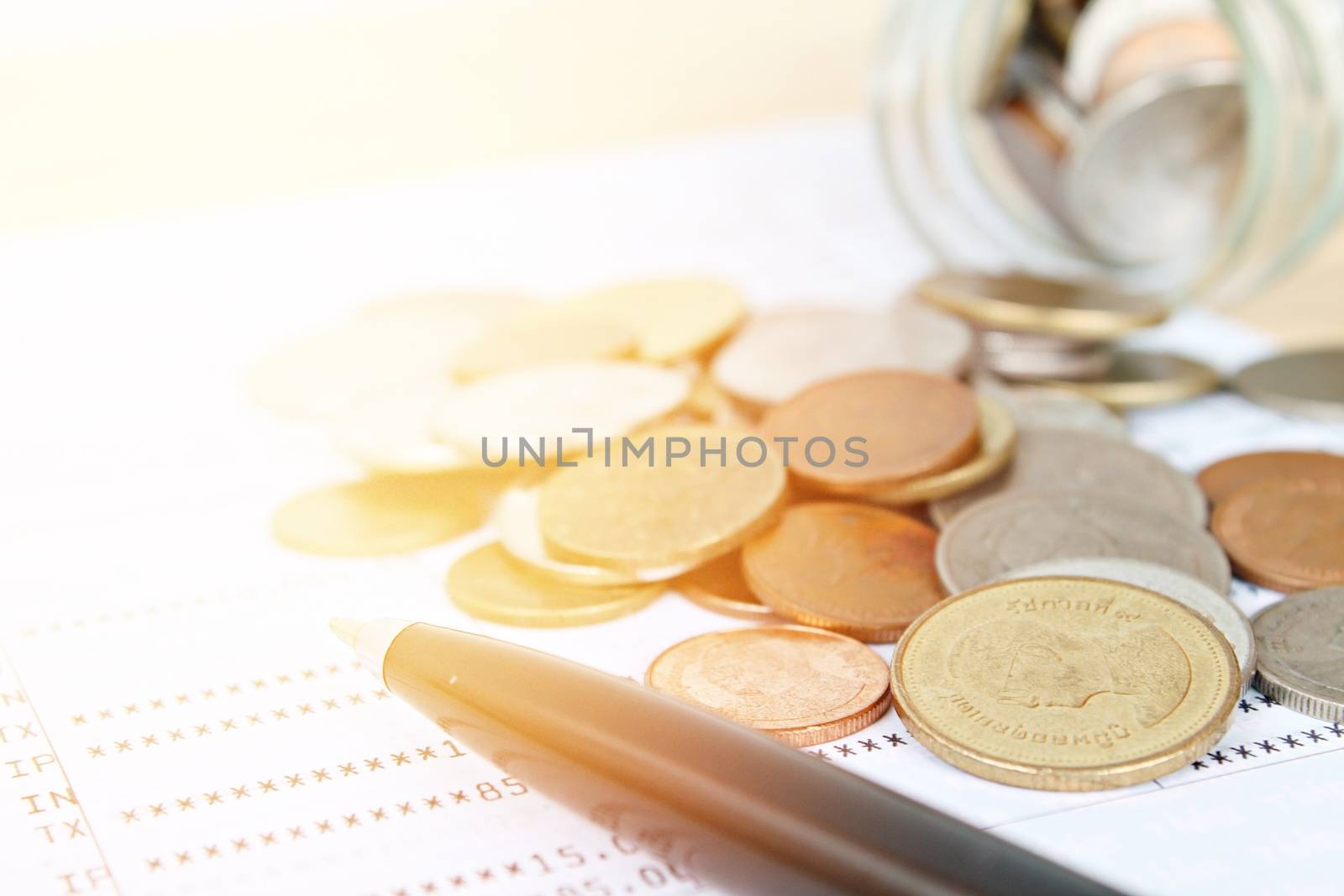 Business, finance, saving money, banking, loan, investment, taxes or accounting concept : Coins scattered from glass jar and pen on saving account book or financial statement