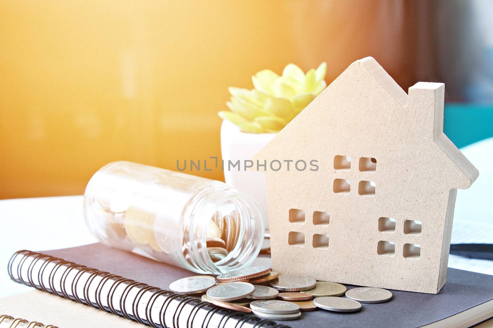 Business, finance, savings, property ladder, mortgage or loan concept : Wood house model and coins scattered from glass jar on notebook paper