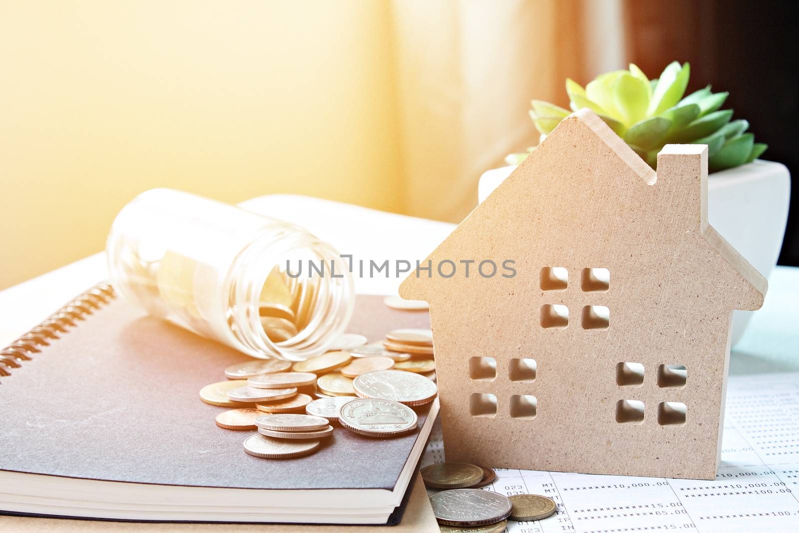 Business, finance, saving money, banking, property loan or mortgage concept :  Wood house model and coins scattered from glass jar on office desk table