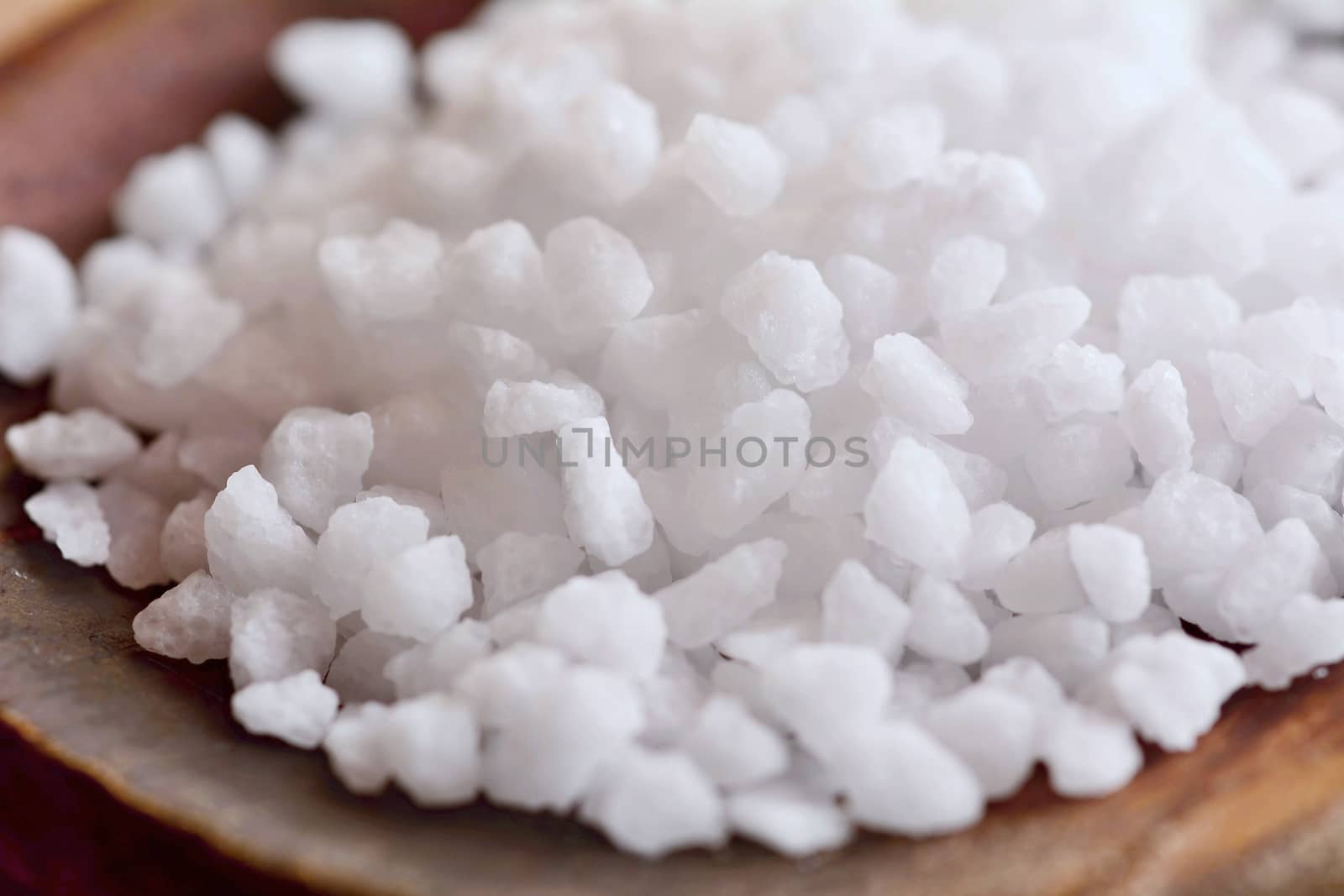 Macro shot of a white clear salt crystals on a wooden spoon.