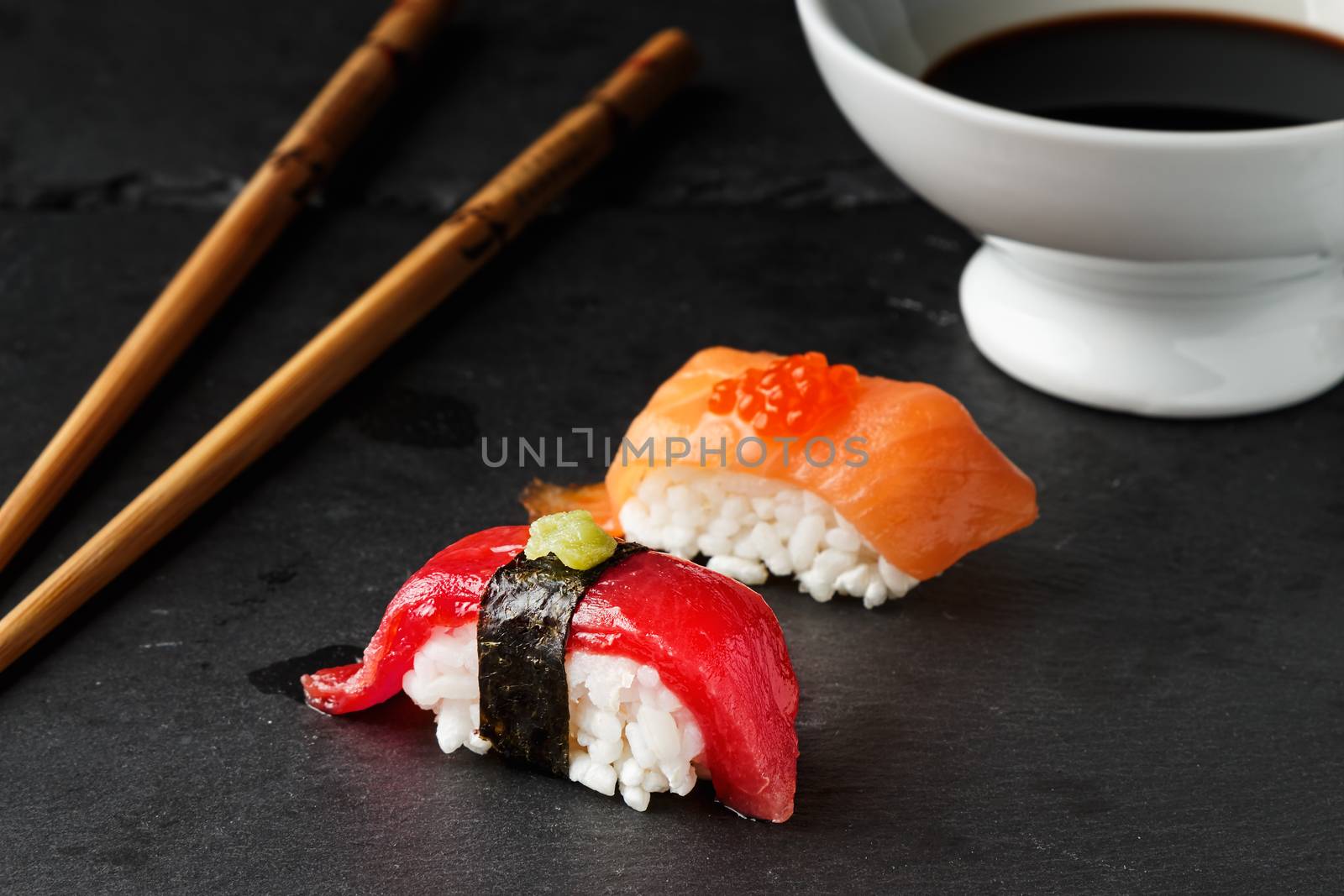  Red tuna Nigiri with Nori seaweed and wasabi paste on black slate stone with chopsticks and bowl of soy sauce. Raw fish in traditional Japanese sushi style. Horizontal image.