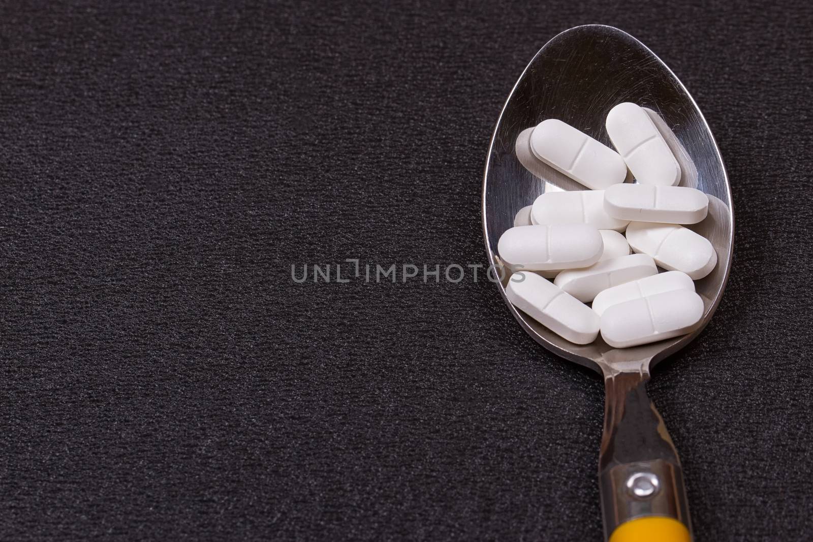 Assorted pharmaceutical medicine pills, tablets and capsules on wooden spoon. black background