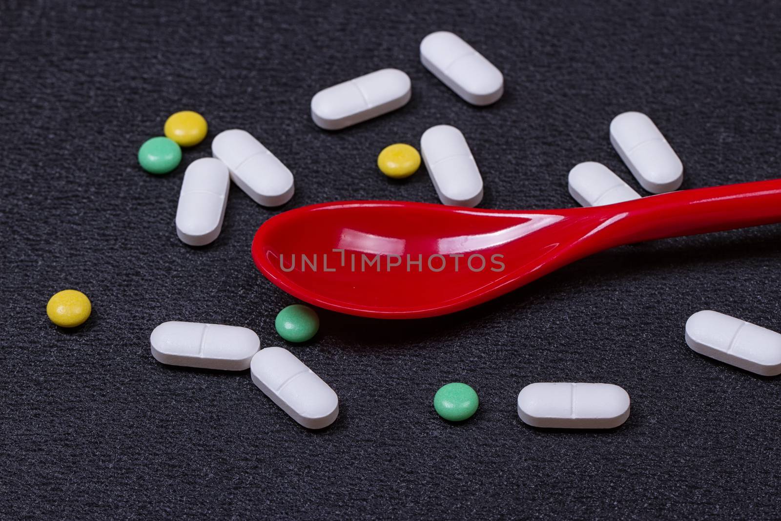 Assorted pharmaceutical medicine pills, tablets and capsules on wooden spoon. black background