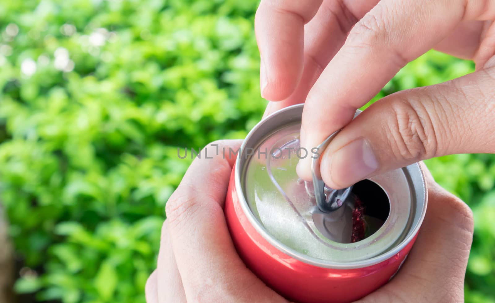 Closeup woman's hand open cola can with nature green blackground