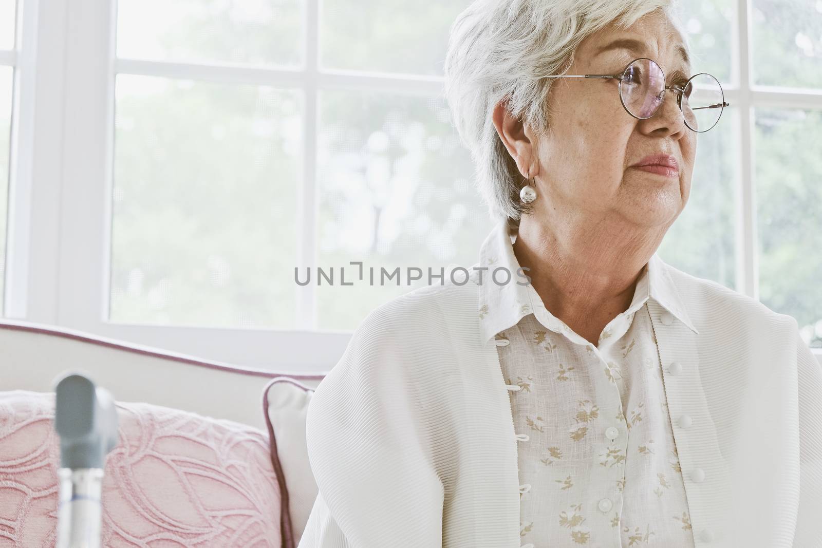 senior woman portrait, senior woman sitting alone on a sofa at home in a lonely mood.