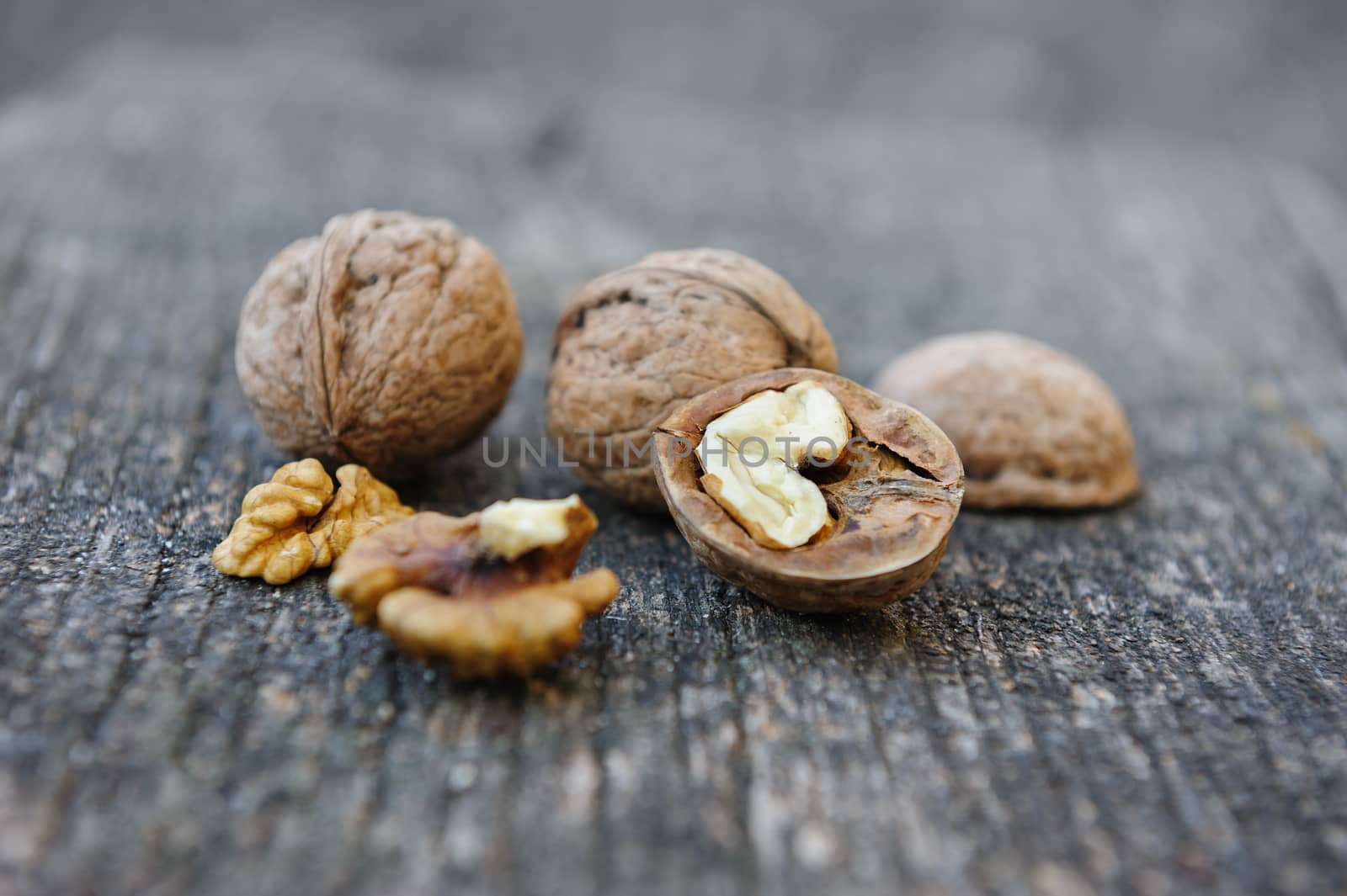 Whole and cracked walnuts at old wooden plank. Still life with selective focus.