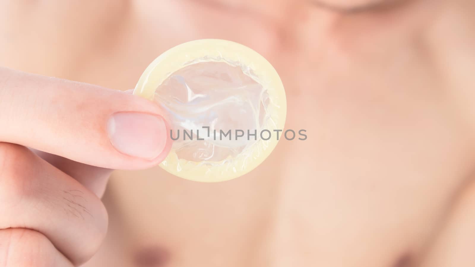 Hand hold condom with blurred man background for AIDs awareness  by pt.pongsak@gmail.com