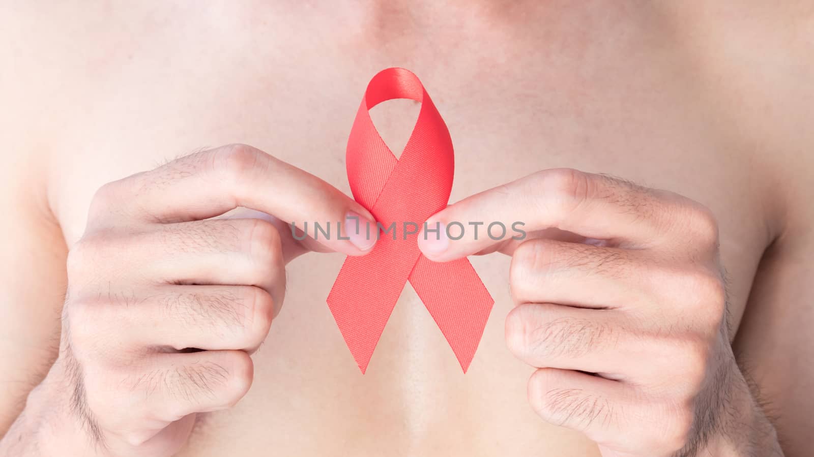 Hand hold red ribbon with blurred man background for AIDs awareness concept