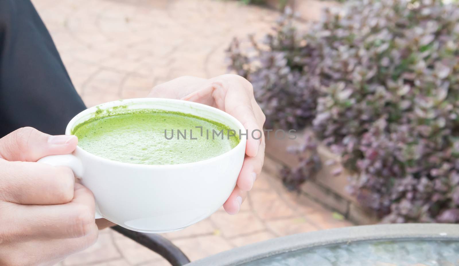 Woman hand holding a cup of hot matcha latte or green tea with nature background