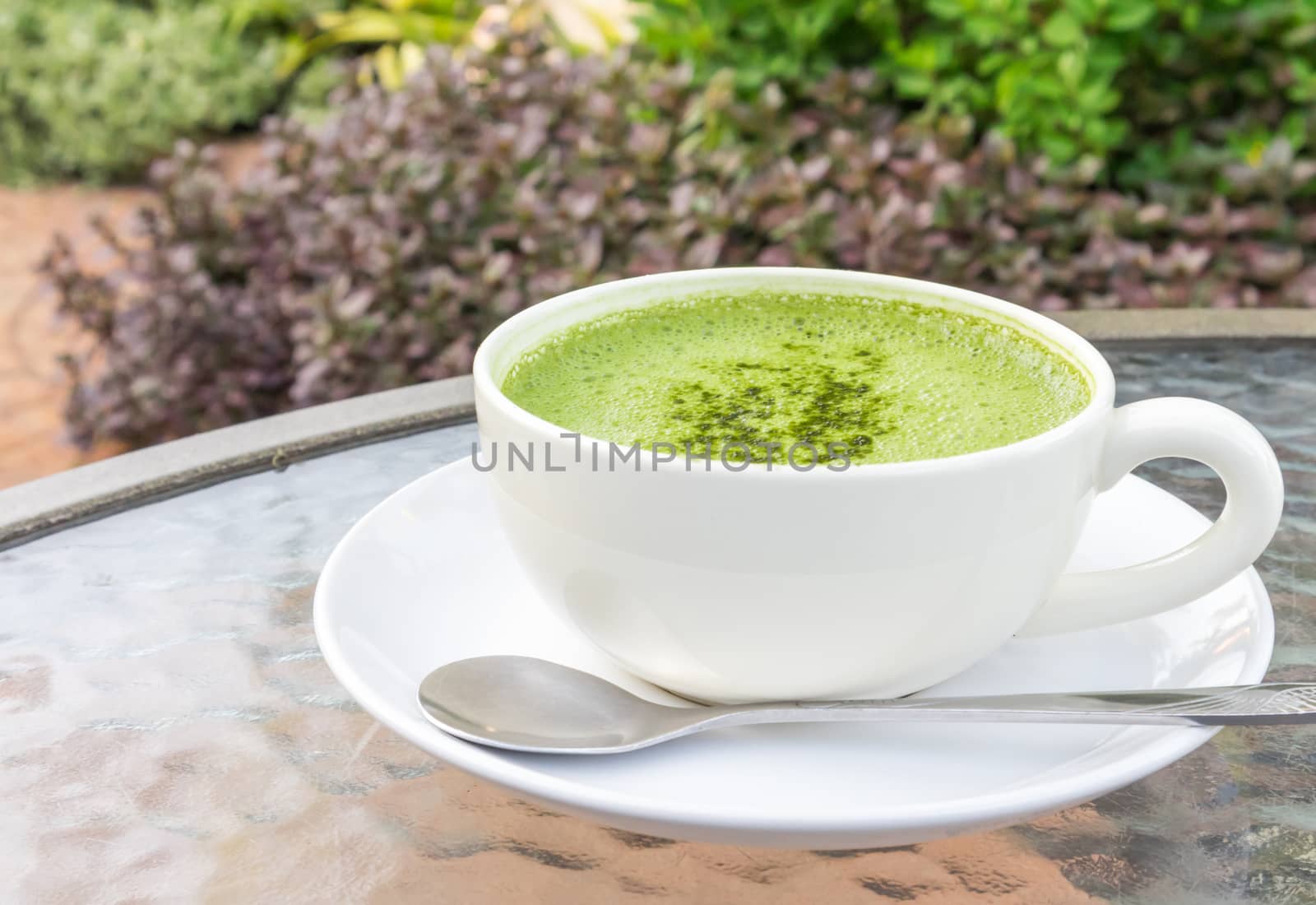 Closeup a cup of matcha latte or green tea on glass table with nature background