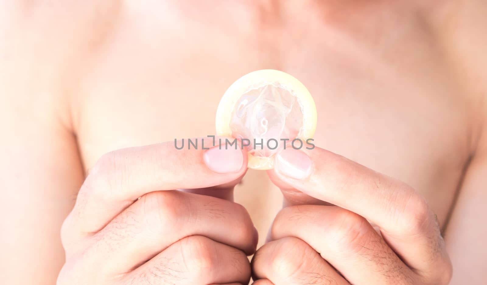 Hand hold condom with blurred man background for AIDs awareness concept