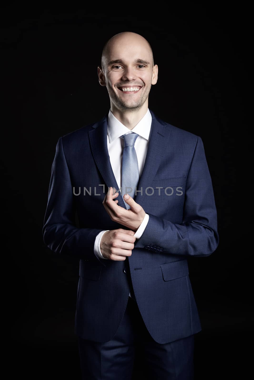 Smiling man fixing cuffs his suit. Studio shot of black background.