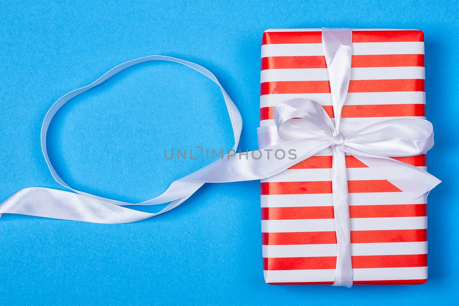 Gift in red and white packing with ribbon on a blue background. a Christmas gift