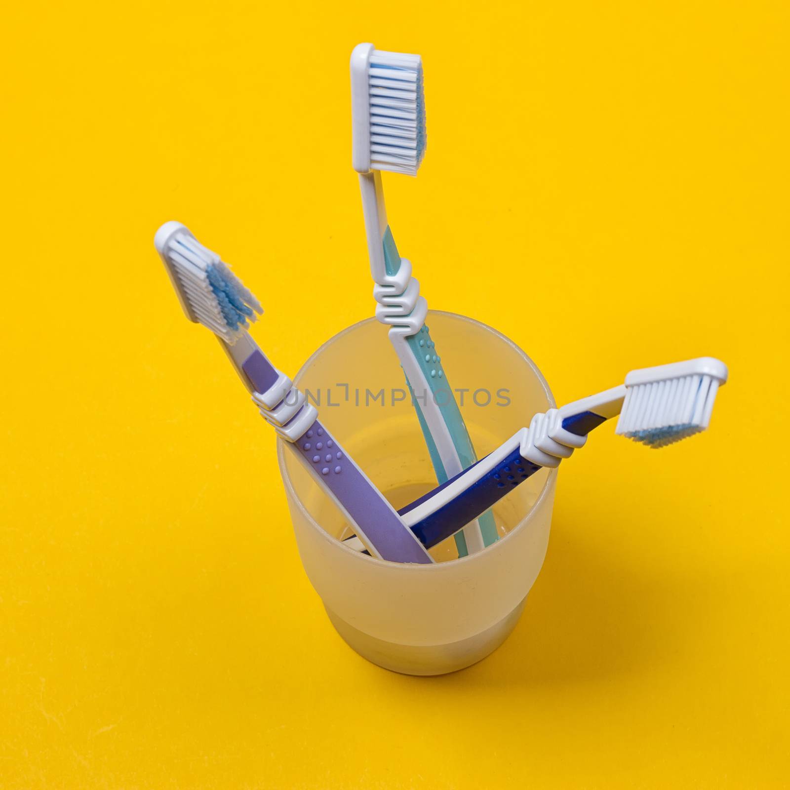 three toothbrushes in a glass on the yellow background. Top view