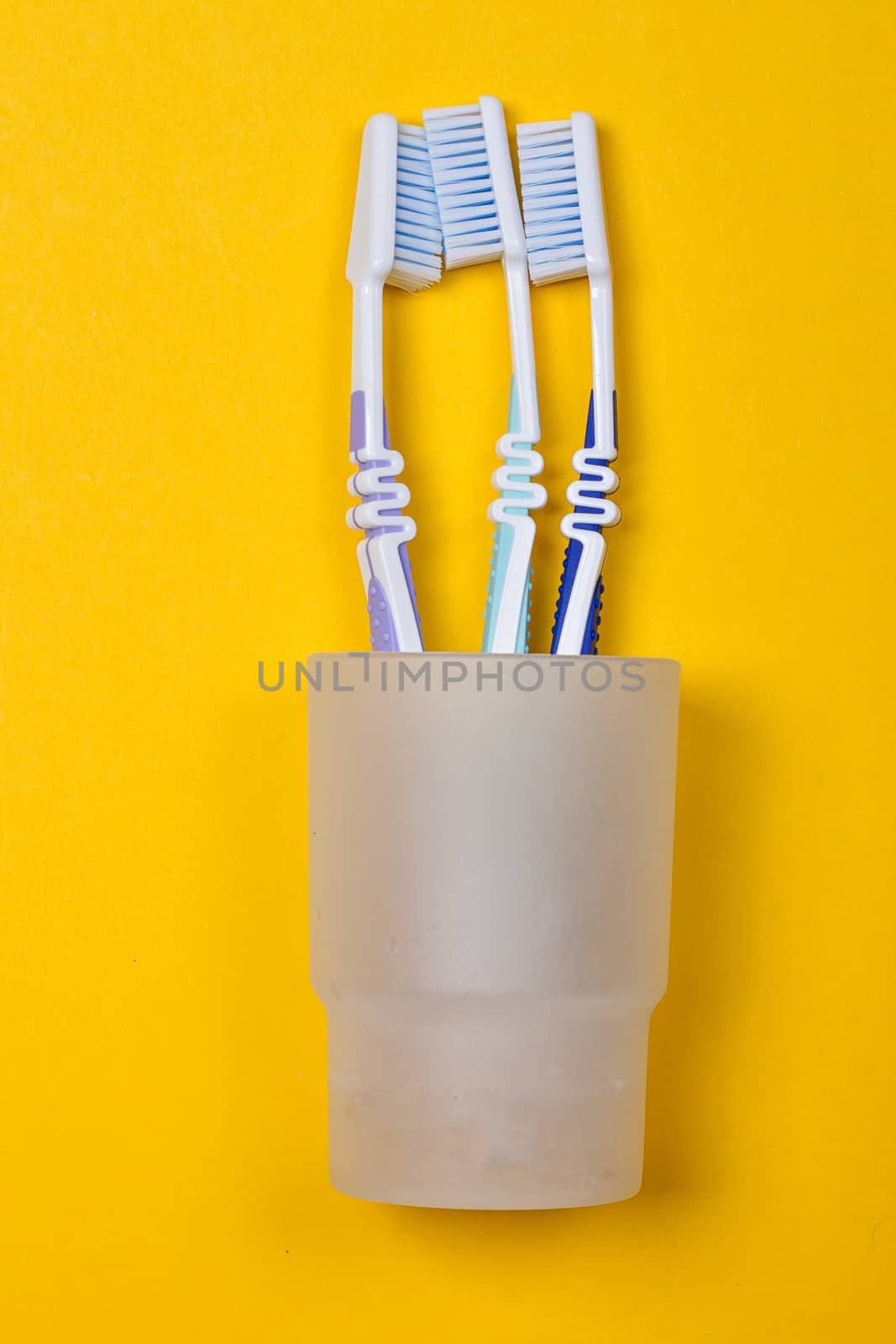 three toothbrushes in a glass on the yellow background. Top view