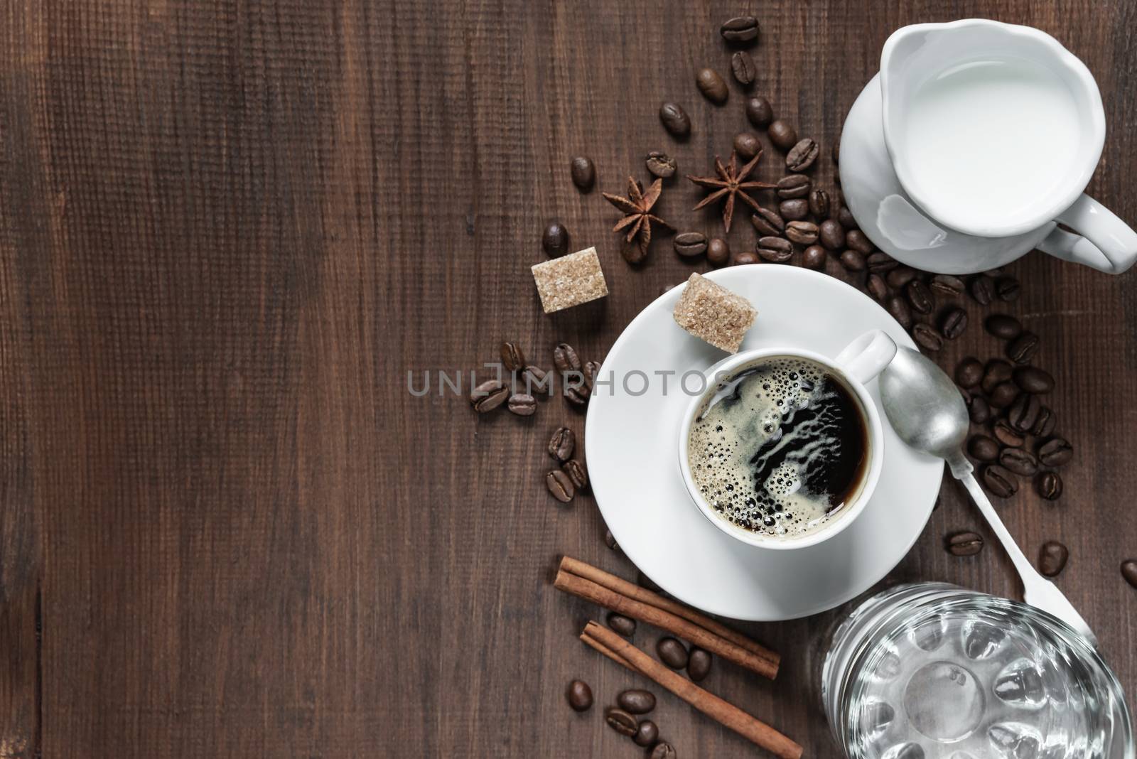 Cup of coffee, cream in a milk jug, glass of water and various spices on the wooden table with copy-space, top view