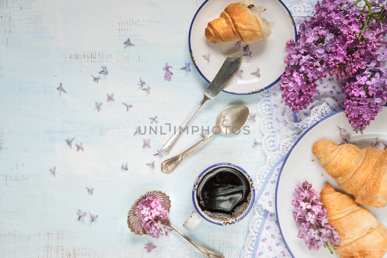 Spring breakfast with a cup of black coffee, croissants and lilac flowers, with space for text