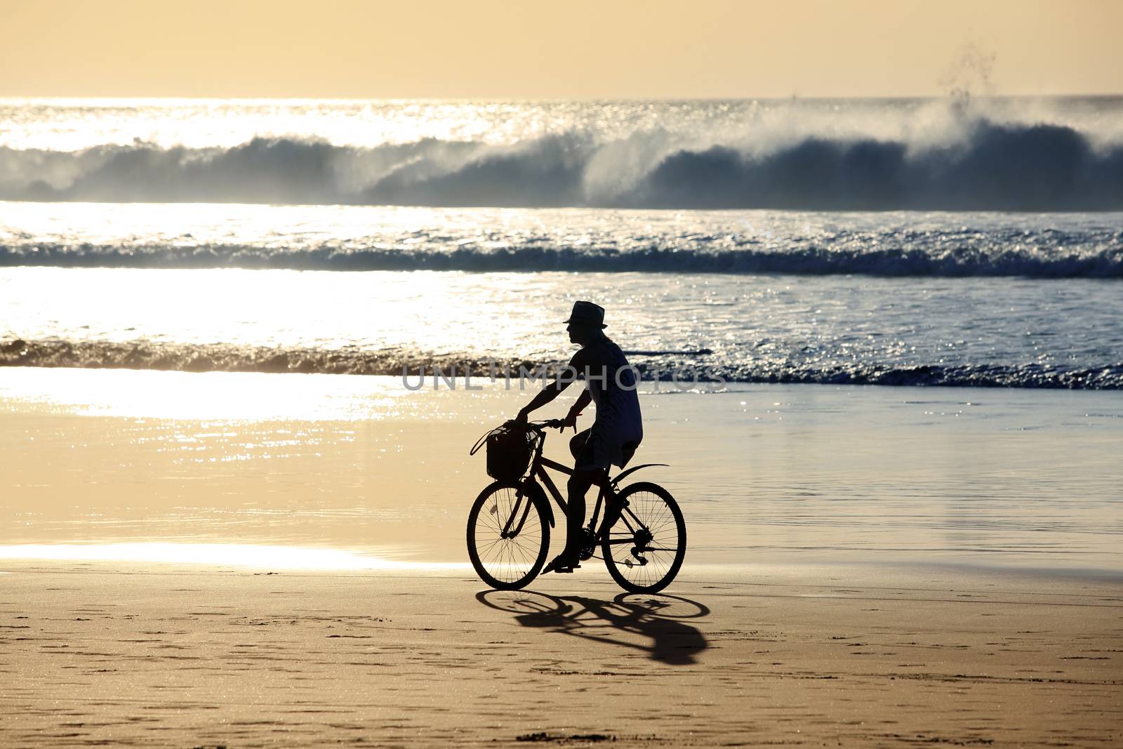 A girl on a bicycle is riding along the ocean at sunset. Bali, Indonesia
