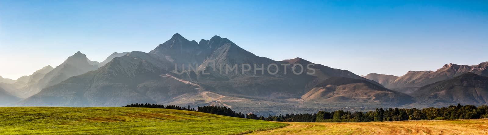 panorama of Tatra mountains in evening haze behind the forest and rural field
