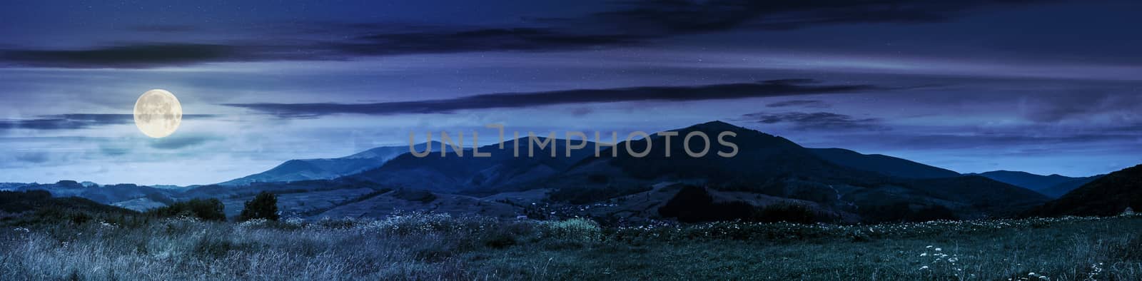 Summer landscape panoramic image of rural fields in mountains under cloudy sky at night in full moon light