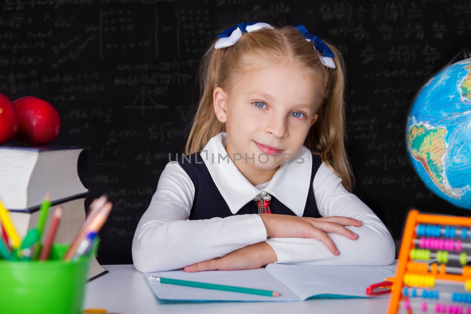 Cute schoolgirl girl with books near school blackboard