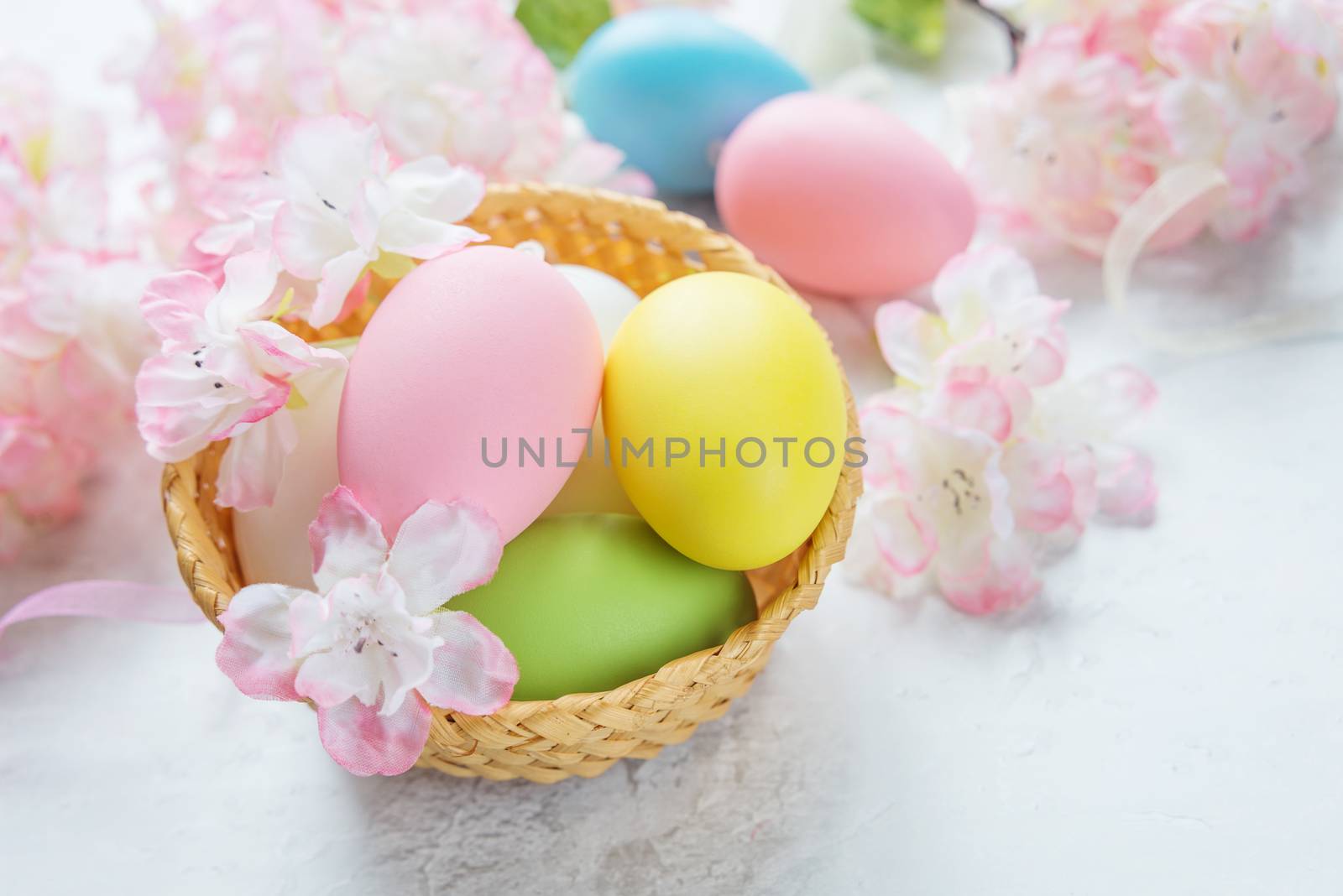 Easter composition with multicolored easter eggs in a wicker basket on the background of delicate pink flowers of the cherry blossoms