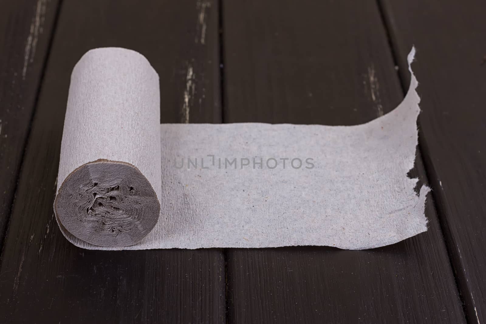 The roll of grey toilet paper on the black wooden background