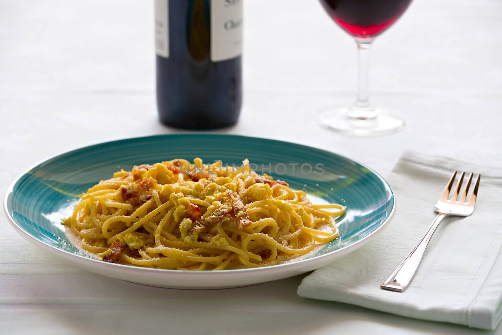 Spaghetti carbonara with egg, smoked bacon and cheese over a table with a wine glass