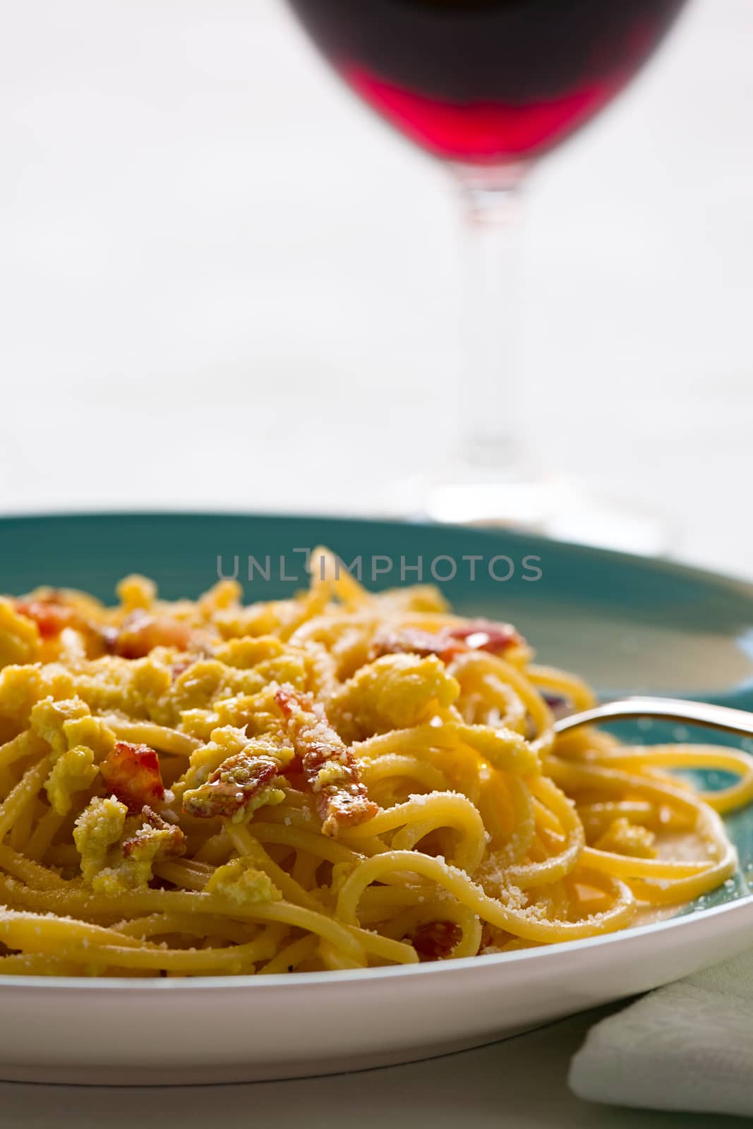 Closeup of spaghetti carbonara with egg, smoked bacon and cheese over a table with a red wine glass