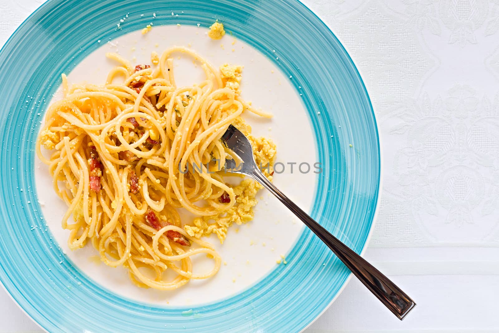 Closeup of eaten spaghetti carbonara with egg, smoked bacon and cheese over a table seen from above