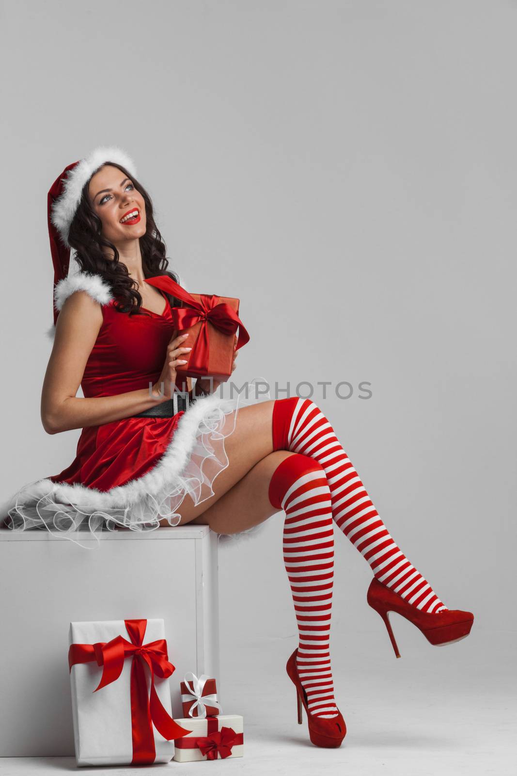 Beautiful young pin-up girl in santa dress unwrapping a christmas present