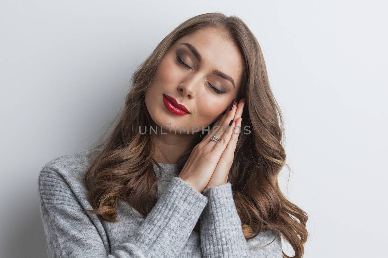 Beautiful young woman holding her hands on her chick and dreaming with eyes closed