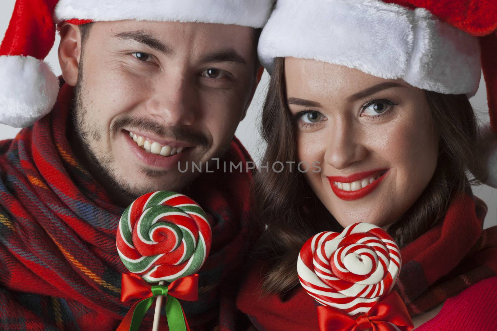 Young happy funny couple in christmas santa hats with lollipops