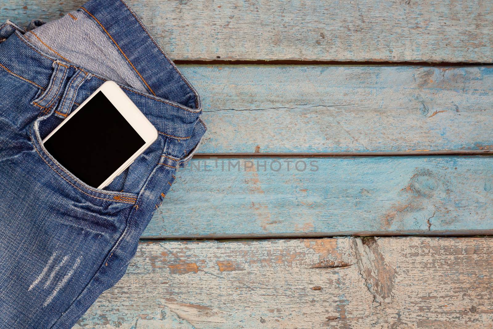 Touch smartphone-phone with headphones in jeans pocket on blue wooden background.