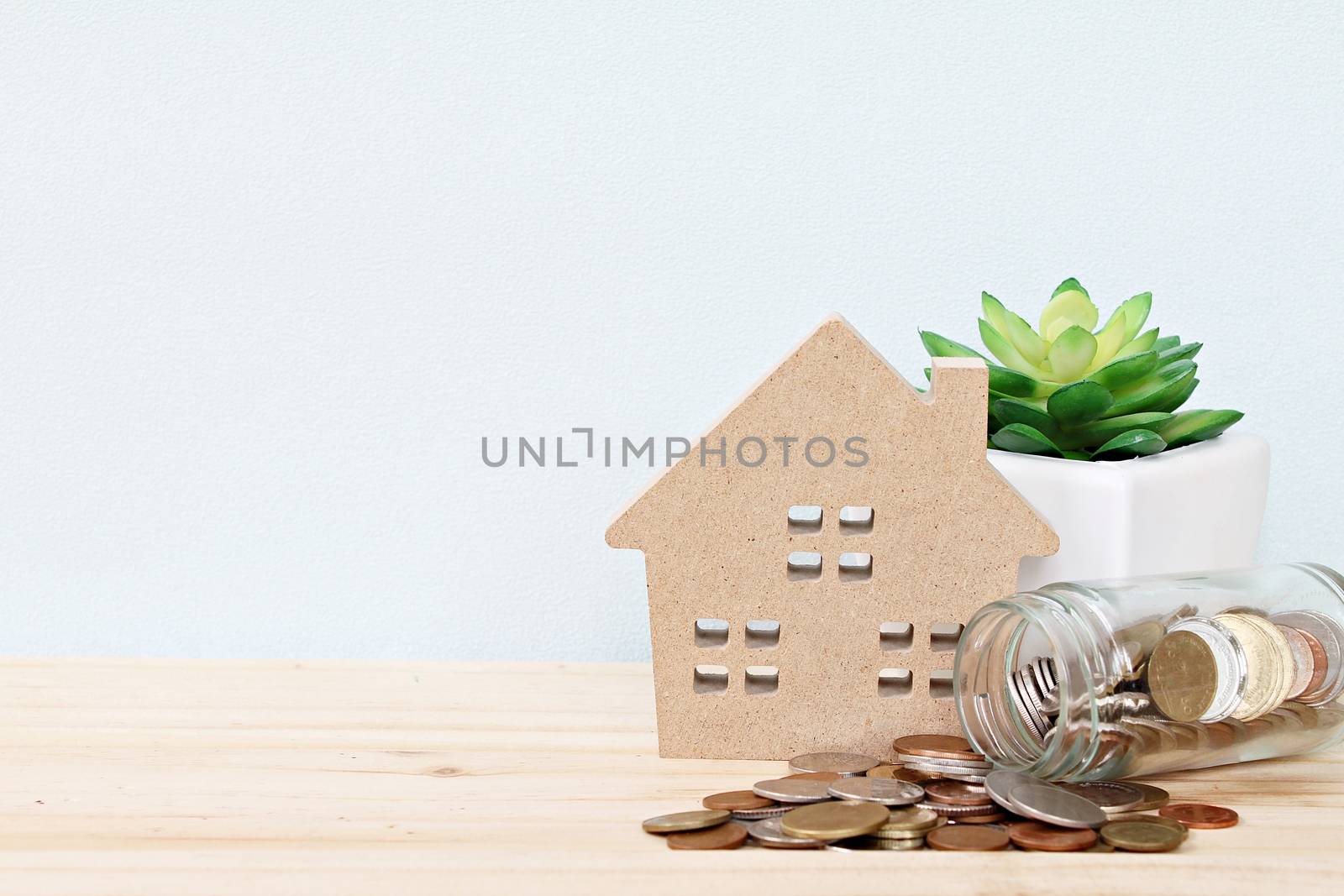 Business, finance, saving money, property ladder or mortgage loan concept : Wood house model, coins scattered from glass jar on desk table